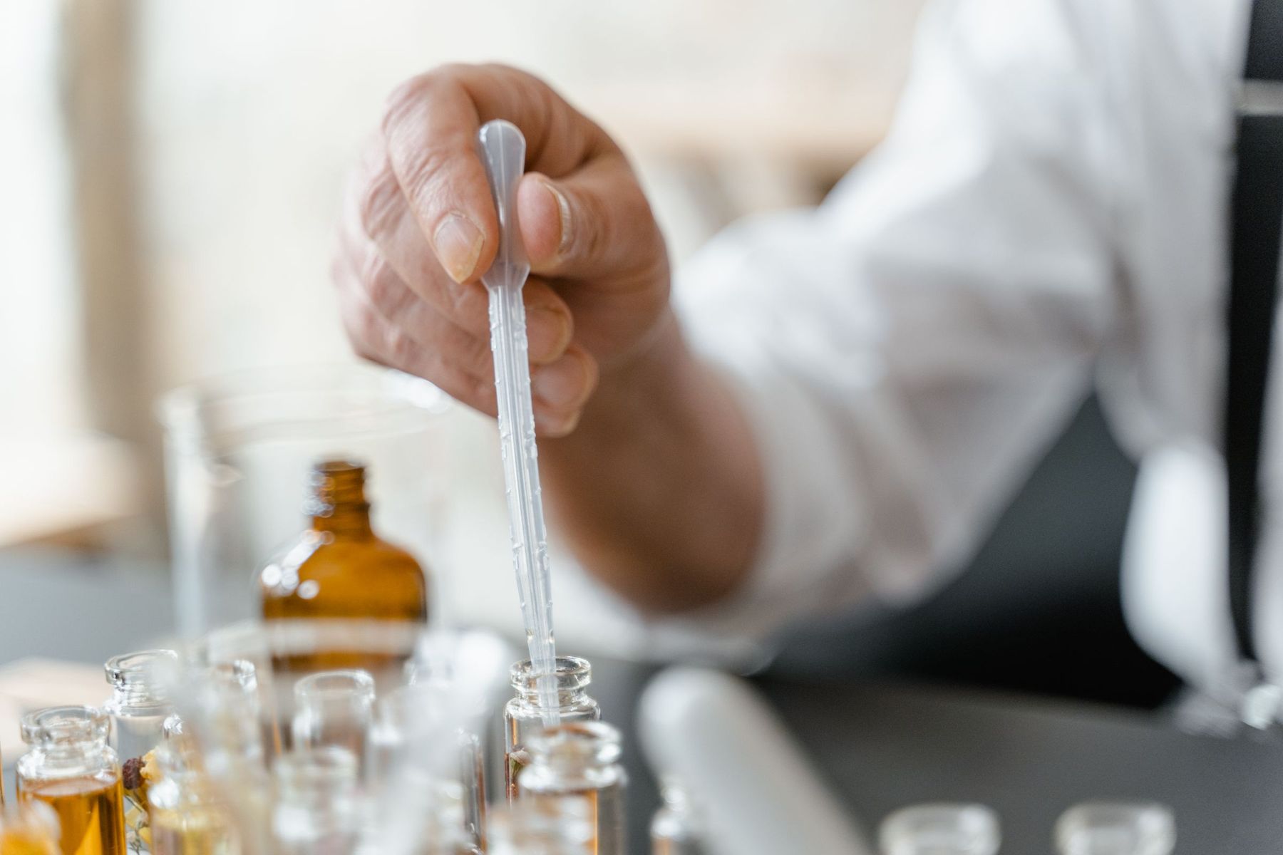 A pipette above vials of fragrance materials